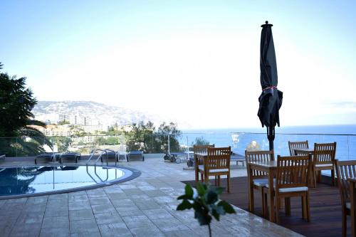 a patio with a pool and chairs and an umbrella at Madeira Regency Cliff - Adults Only in Funchal