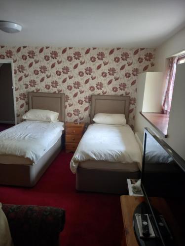two beds in a room with floral wallpaper at The Castle Inn in Ebbw Vale