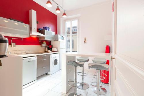 a kitchen with red walls and white counters and stools at Cosy apartment 39M2, two steps from rue d'Antibes and Croisette in Cannes