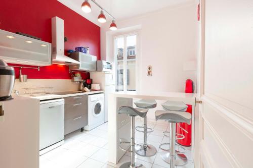une cuisine avec des murs rouges, des comptoirs et des tabourets blancs dans l'établissement Cosy apartment 39M2, two steps from rue d'Antibes and Croisette, à Cannes