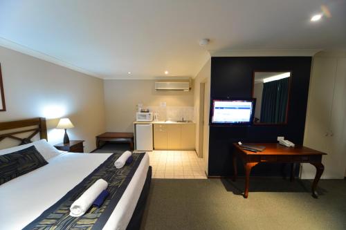 a hotel room with a bed and a desk and a television at Wattle Grove Motel in Perth