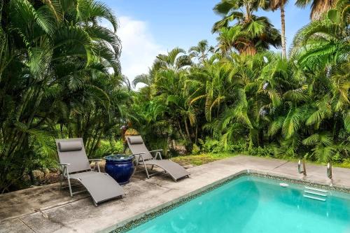 a swimming pool with two chairs and palm trees at Kona Sunset House at Walua in Kailua-Kona