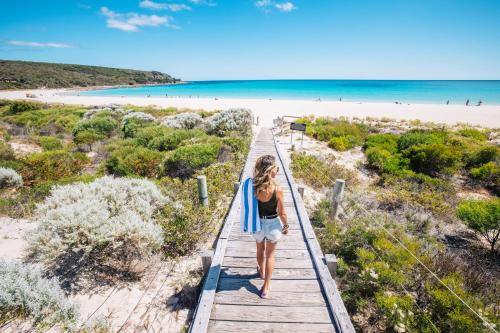 a woman walking down a beach with a surfboard at Pullman Bunker Bay Resort Margaret River in Dunsborough