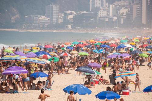 eine große Gruppe von Menschen am Strand mit Sonnenschirmen in der Unterkunft Hotel Vitória in Rio de Janeiro