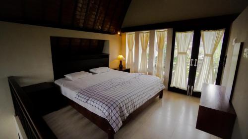a bedroom with a bed with a checkered blanket and windows at The Janan Villa in Sanur