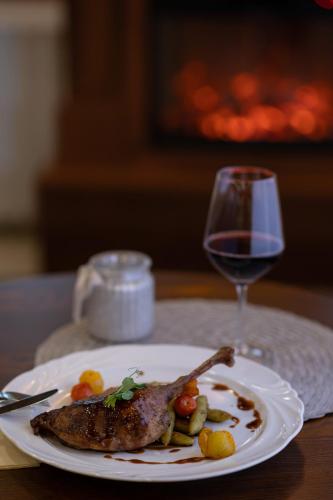 a plate with a piece of meat and a glass of wine at Kőkapu Vadászkastély és Hotel & Apartments in Nagyhuta