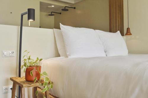 ein weißes Bett mit weißen Kissen und einer Pflanze auf einem Tisch in der Unterkunft Van Heeckeren Apartments & Suites Nes in Nes