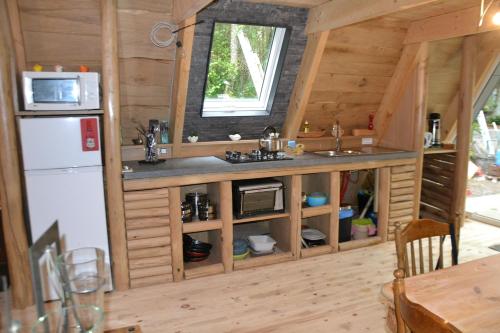 a kitchen in a log cabin with a sink and a refrigerator at La Bulle Du Trappeur (Chevaux bienvenus) in Pondrôme