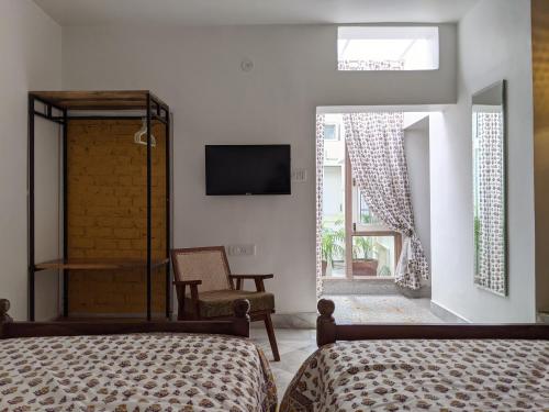 1 dormitorio con 2 camas, TV y silla en Mukam, Boutique Homestay, en Jaipur