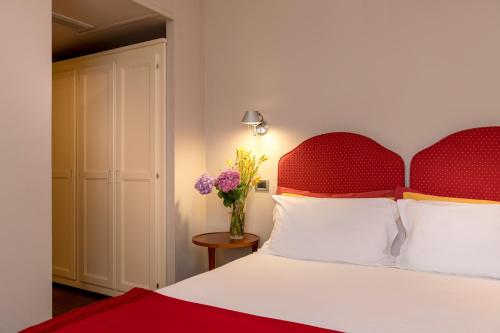 a bed with a red headboard and a vase of flowers at Bijou Hotel in Saint Vincent