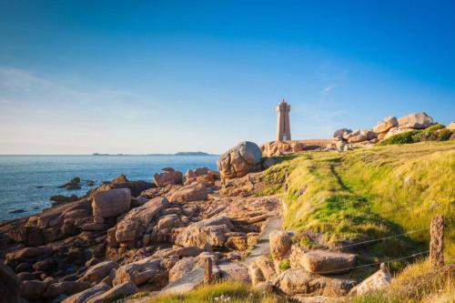a lighthouse on a rocky shore with the ocean at Le Penty du Peulven in Plestin-les-Grèves