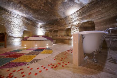 格雷梅的住宿－Göreme Cave Lodge，一间带浴缸、床和地毯的卧室