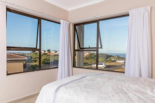 a bedroom with large windows with a view of the ocean at Sun n Surf Sunny and spotless 1 bedroom apartment in Ballito