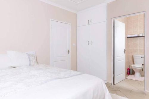 a white bedroom with a white bed and a toilet at Sun n Surf Sunny and spotless 1 bedroom apartment in Ballito