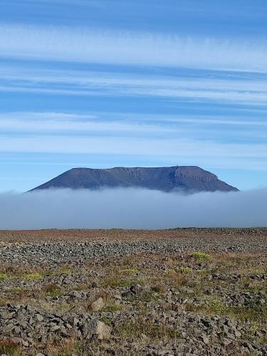 a mountain in the middle of a field with clouds at Happy-Cove Guesthouse - by the sea in Bakkafjörður