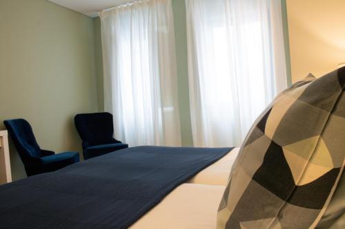 a bedroom with a bed with two chairs and a window at Kavia Hotel do Largo in Cascais