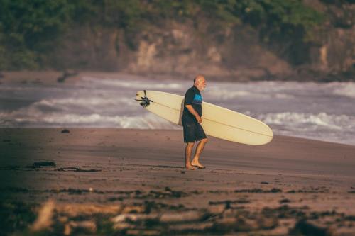 a man standing on the beach holding a surfboard at Hostal Los Chamos in San Juan del Sur