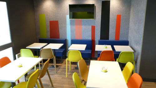 a dining room with white tables and colorful chairs at ibis budget Lisieux in Lisieux