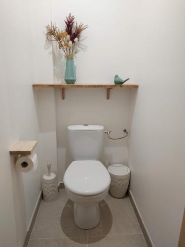 a white bathroom with a toilet and a vase of flowers at La ferme des Escampades in Monteux