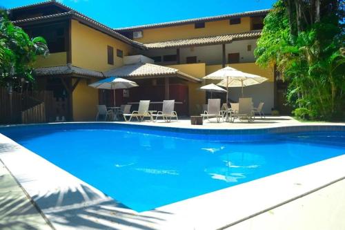 una piscina frente a una casa con sillas y sombrillas en Paz & Diversão Praia Do Forte, en Praia do Forte