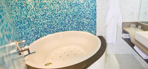 a bath tub in a bathroom with a mosaic wall at WestCord Hotel Schylge in West-Terschelling
