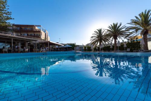 ein großer Pool mit Palmen im Hintergrund in der Unterkunft Minos Hotel in Rethymno