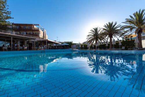 a large swimming pool with palm trees in the background at Minos Hotel in Rethymno