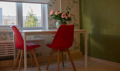 two red chairs sitting at a desk with a vase of flowers at Nameja Apartments in Jēkabpils