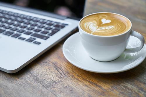 a cup of coffee on a plate next to a laptop at Premier Hotel O.R. Tambo in Kempton Park