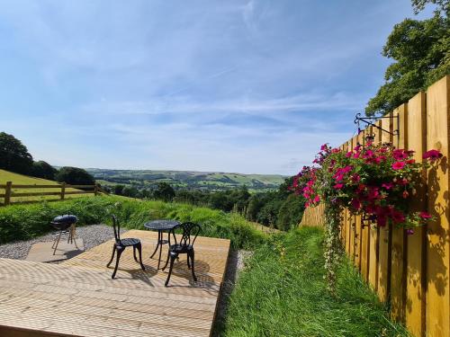 a wooden deck with chairs and a table and flowers at Peak District Shepherds Hut in Hope