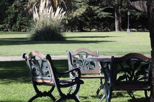 two park benches sitting next to a table in a park at Hotel Colonial San Nicolás in San Nicolás de los Arroyos