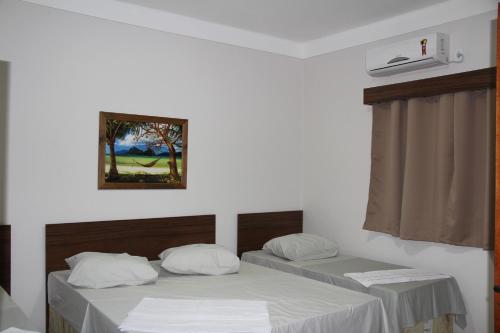 two beds in a room with white sheets and a window at Hotel Joia Fina in Aparecida