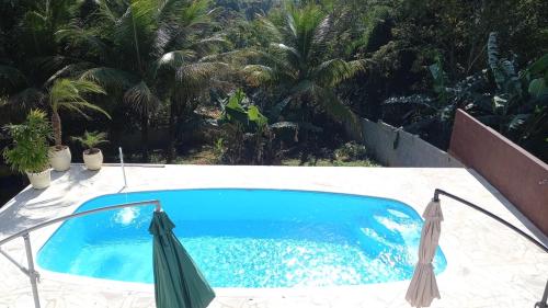 una piscina azul con 2 sombrillas y palmeras en Casa Vista Ilhabela com piscina e wi-fi, en Ilhabela