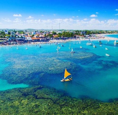 a boat with a yellow sail in the water near a beach at Suítes Cavalo Marinho in Porto De Galinhas