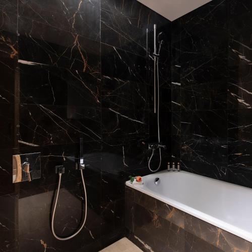 a black tiled bathroom with a tub and a shower at The Bentley Luxury Hotel & Suites in Doha