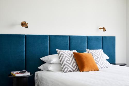 Astina Suites, Penrith في بينريث: سرير مع اللوح الأمامي الأزرق والوسائد البيضاء