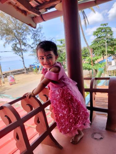a little girl in a pink dress leaning on a fence at Sajeev Home Stay in Cherai Beach