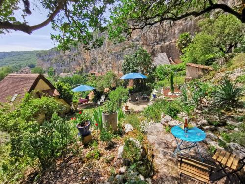 a garden with a blue table and blue umbrellas at Gîtes Un Jardin dans la Falaise in Cabrerets