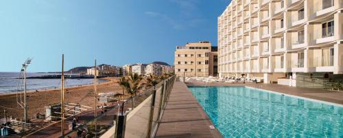 a swimming pool next to a beach next to a building at Hotel Cristina by Tigotan Las Palmas - Adults Only in Las Palmas de Gran Canaria