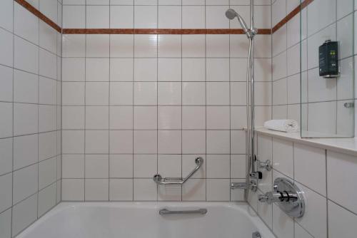 a white tiled bathroom with a tub and a shower at Seminaris Hotel Bad Boll in Bad Boll
