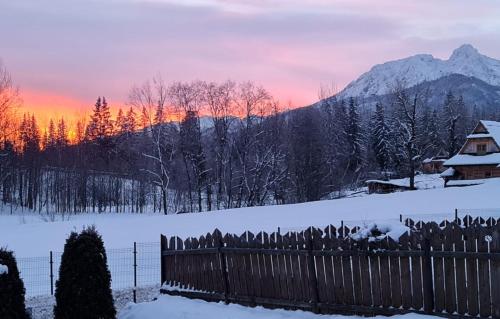 a fence in a snowy field with a sunset at Czarne jagody in Kościelisko