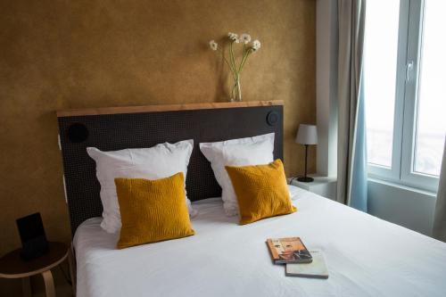 a bed with yellow pillows and a book on it at Hôtel La Nouvelle République & Hammam in Paris