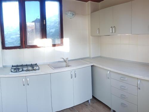 kuchnia z białymi szafkami, umywalką i oknem w obiekcie Casa Maxim w mieście Sulina