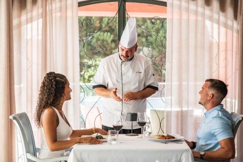 a chef standing in front of a table with two people at Boutique Hotel Vivenda Miranda in Lagos