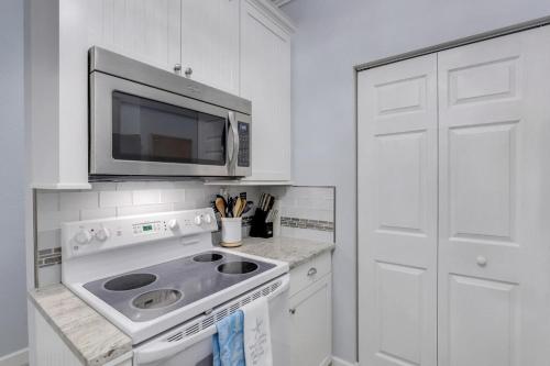 a white kitchen with a microwave and a stove at Charming condo with two pools and steps to beach in Marco Island