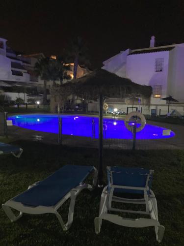 two chairs and an umbrella next to a swimming pool at night at La Hacienda Golf Islantilla AIRE ACONDICIONADO Y WIFI -SOLO FAMILIAS Y PAREJAS- in Islantilla