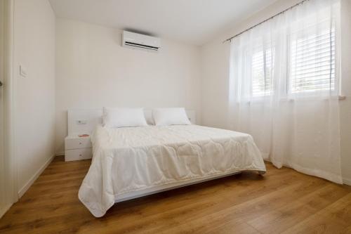 a white bedroom with a bed and a window at Apartmani Vuletić in Neum