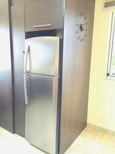 a stainless steel refrigerator in a kitchen with a clock on the wall at Eco Hotel Katarma in Puerto Baquerizo Moreno