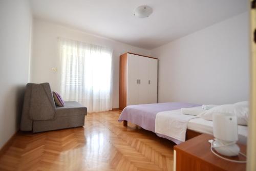 a bedroom with a bed and a chair and a window at Apartmani Badurina - Crnika in Lun
