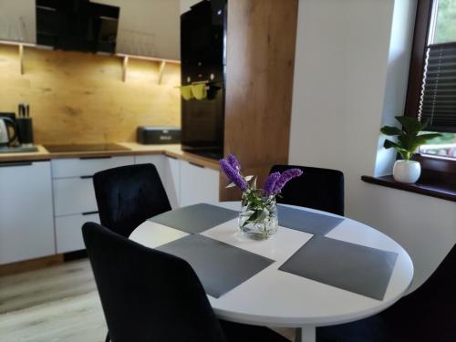 a white table with a vase of purple flowers on it at Apartament Szumi Las Kletno in Kletno